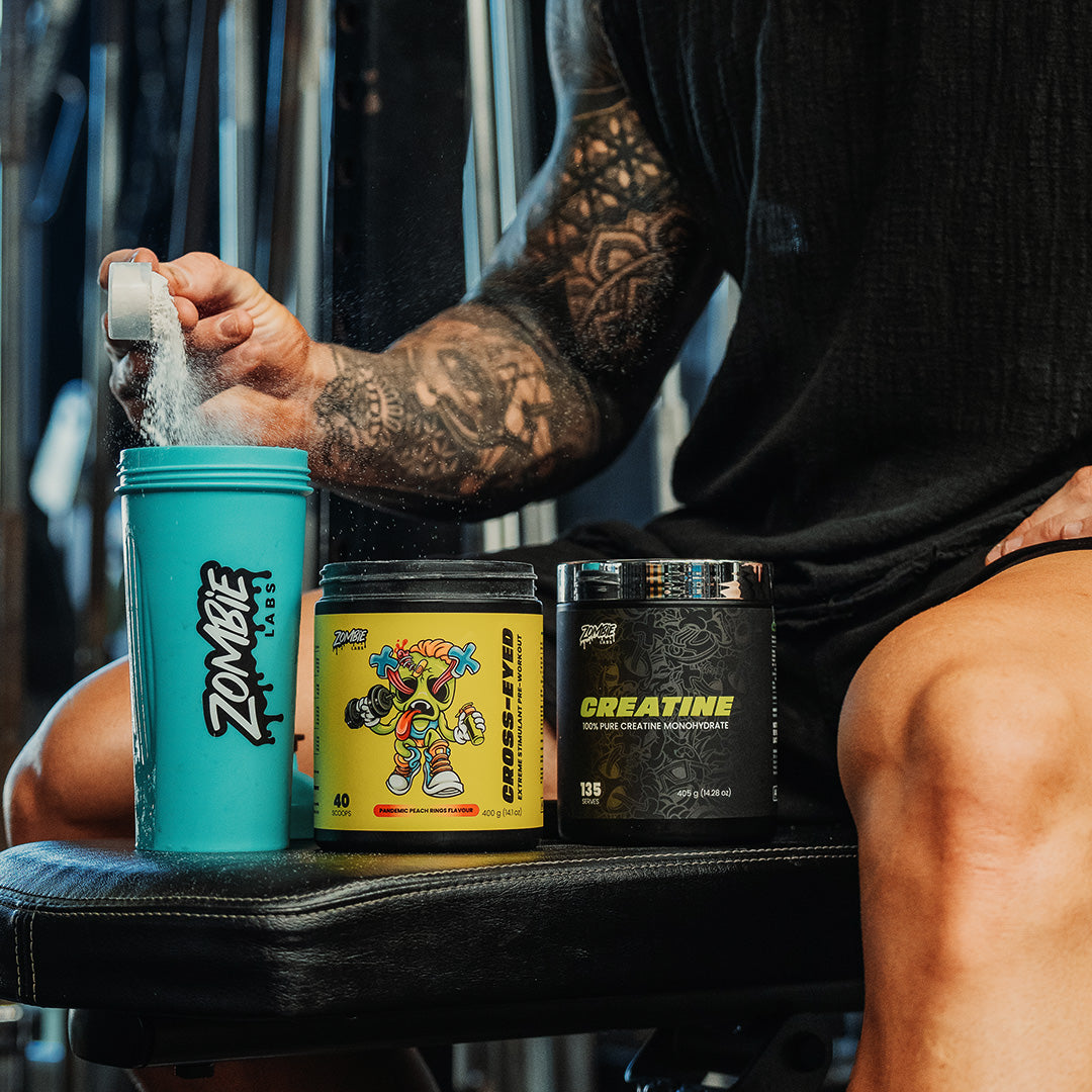 Zombie Labs Cross-eyed pre workout and creatine being mixed in a shaker by a muscular male sitting on a weight bench.