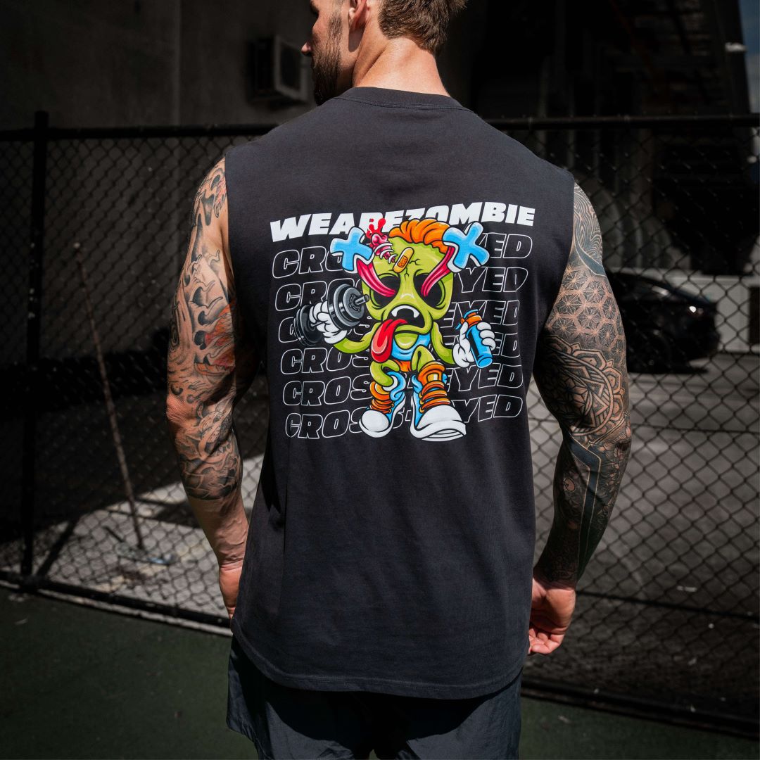 A man with tattooed arms standing outdoors, showing the back of his black Zombie Labs sleeveless tank top featuring a colorful cartoon character and 'WEAREZOMBIE CROSSEYED' text.