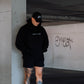 A man leaning against a concrete structure wearing a black Zombie Labs hoodie with ZOMBIE LABS on the front.