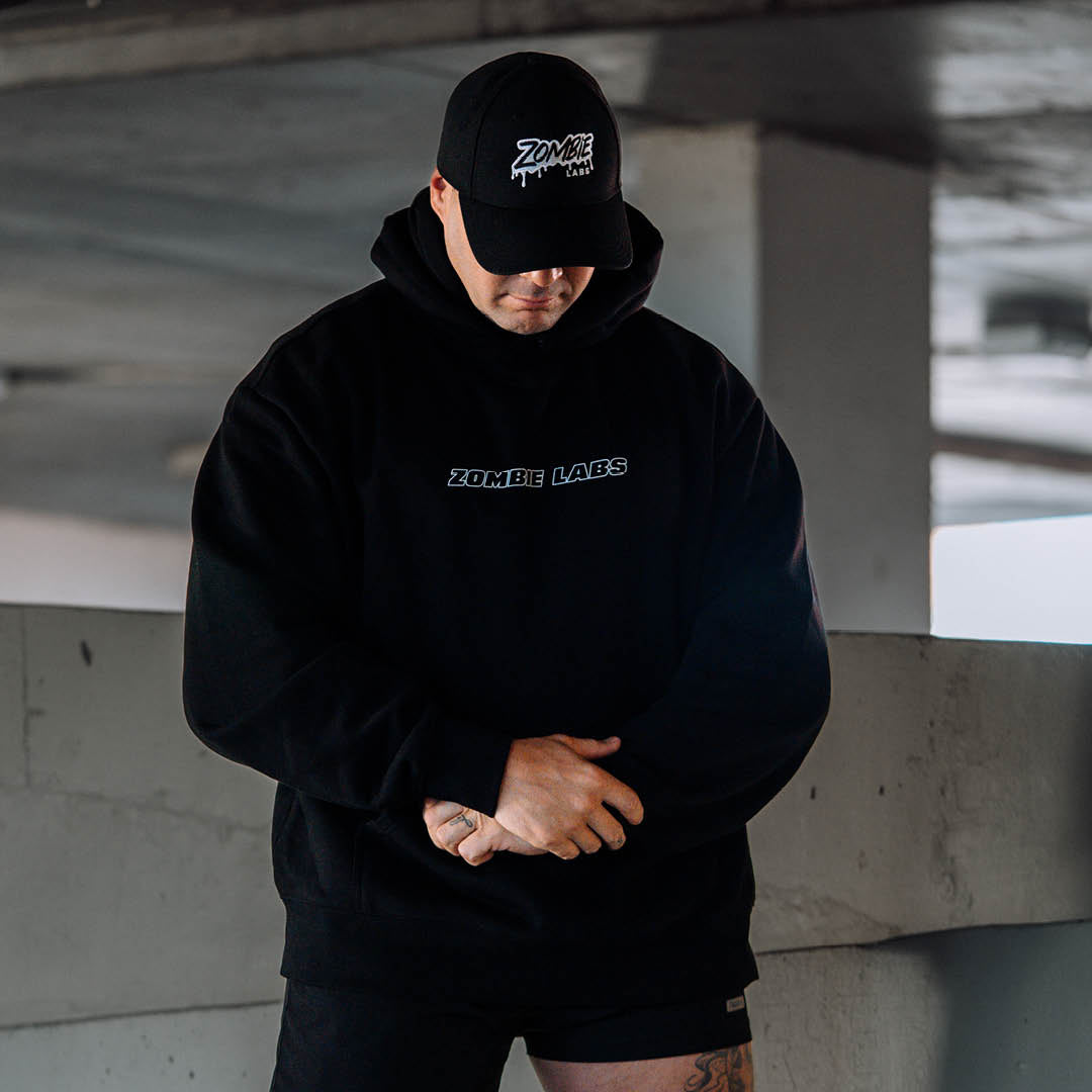 A man looking down wearing a black Zombie Labs hoodie. Background is concrete. 