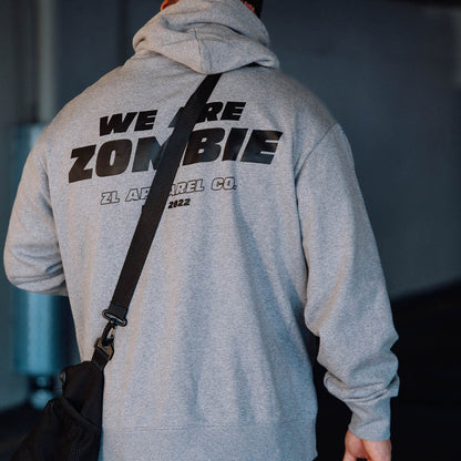 Man wearing a grey Zombie Labs hoodie with 'We Are Zombie' text on the back, carrying a black bag over his shoulder.