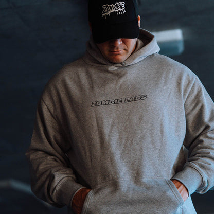 Man wearing a grey Zombie Labs hoodie and cap, looking down with hands in pockets.