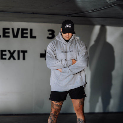 Man wearing a grey Zombie Labs hoodie and cap, standing with arms crossed in a parking garage.